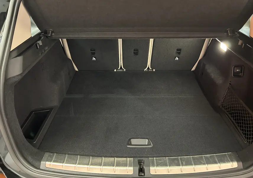 Coffre ouvert vu de l'arrière d'une BMW X1 noire, montrant un espace de chargement propre et bien éclairé.
