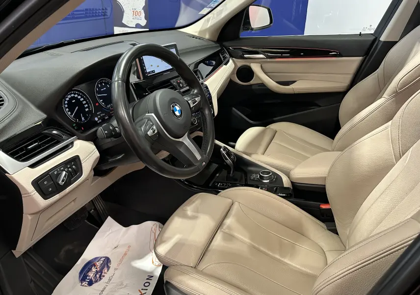 Intérieur beige clair de BMW X1 2019 vu côté conducteur, avec volant noir et tableau de bord digital.