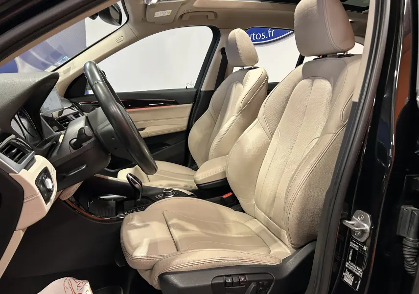 Vue intérieure côté conducteur du BMW X1 noir 2019, sièges en cuir beige et volant multifonction.