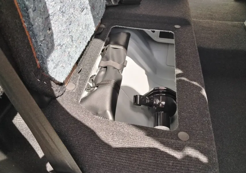 Détail du compartiment de rangement sous le siège arrière du pick-up Isuzu D-MAX blanc, montrant un crochet d'attelage.
