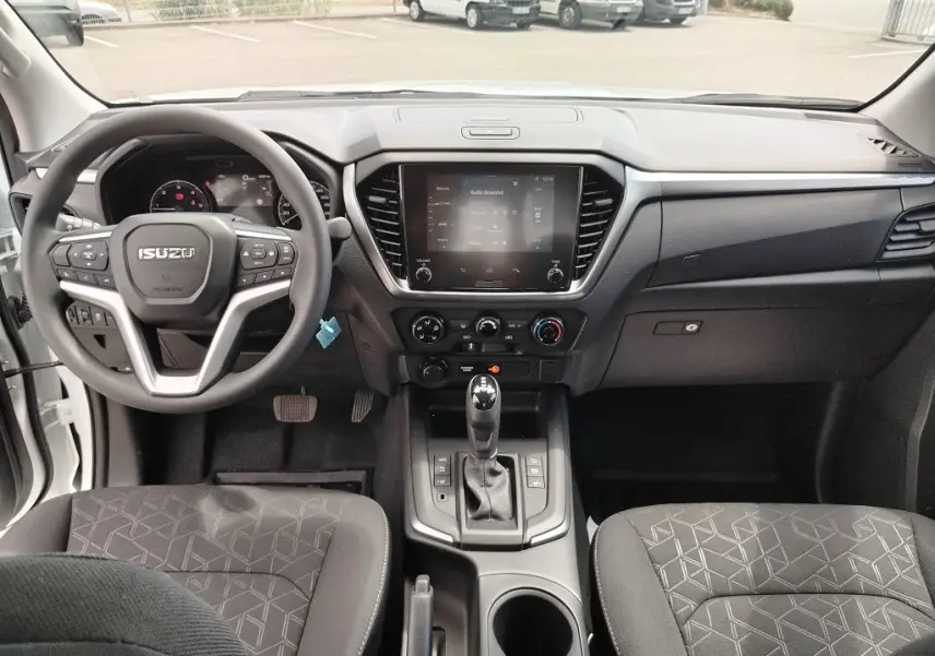 Vue intérieure avant de l'Isuzu D-MAX 2026 avec tableau de bord noir et volant multifonction.