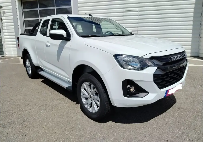 Isuzu D-MAX blanc en 3/4 avant droit, avec arceau et volet couvre benne roulant visible sur un parking extérieur.