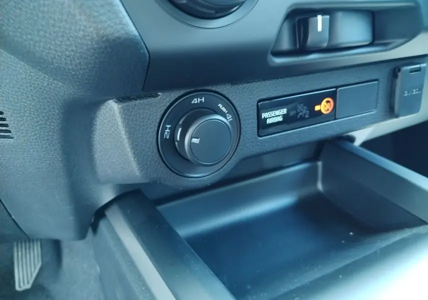 Gros plan intérieur sur le tableau de bord noir de l'Isuzu D-MAX 2026, avec commande de traction 4x4 et témoin airbag passager.