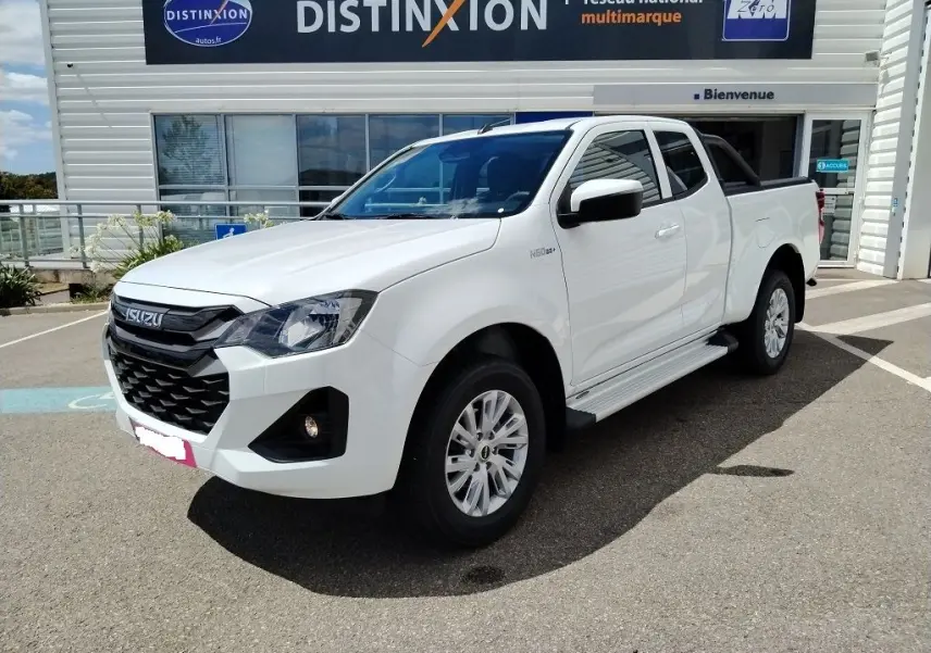 Vue 3/4 avant d'un Isuzu D-MAX blanc avec arceau et couvre benne roulant, stationné devant un bâtiment Distinxion.