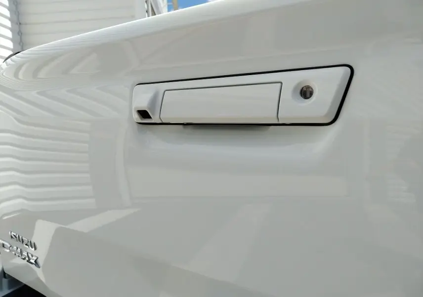 Gros plan sur la poignée blanche de la benne du pick-up Isuzu D-MAX 2026 avec logo visible en bas à gauche.