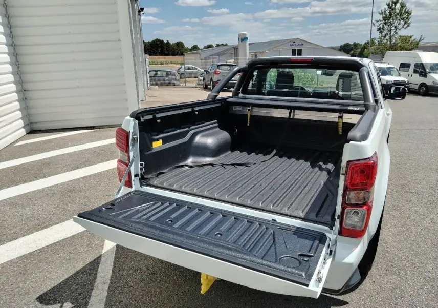 Vue arrière en 3/4 du pick-up Isuzu D-MAX blanc avec benne ouverte, arceau et volet couvre benne roulant visible.
