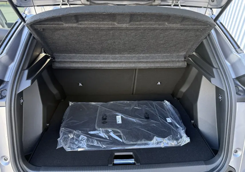 Coffre ouvert vu de l'arrière d'un Peugeot 2008 Hybrid 145 gris Artense avec tapis neufs emballés à l'intérieur.
