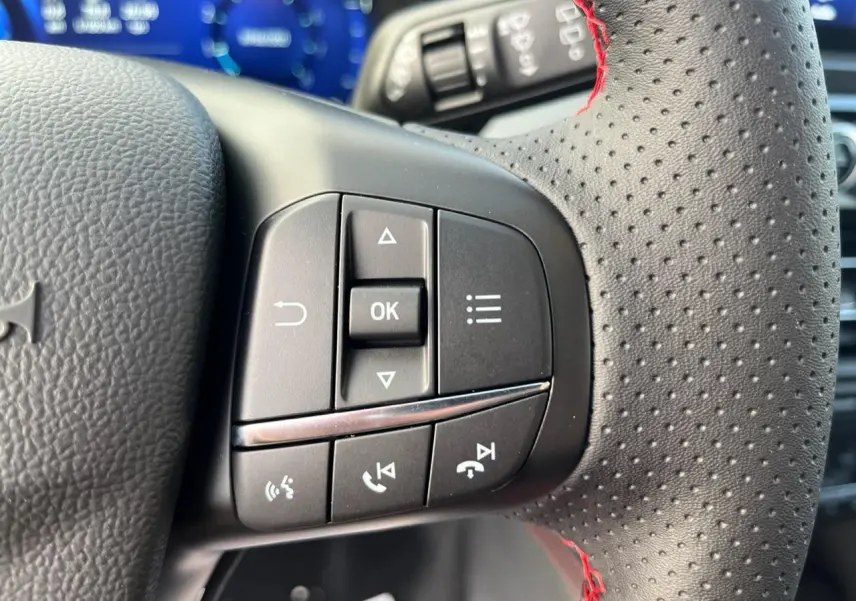 Gros plan sur les commandes du volant perforé avec surpiqûres rouges du Ford Kuga 1.5 EcoBoost 150 ST-Line 2022.