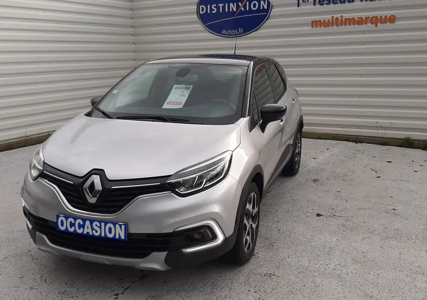 Renault Captur gris avec toit noir, vue 3/4 avant droit, stationné devant un mur blanc avec panneau Distinxion.