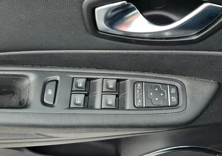 Gros plan sur la commande des vitres électriques et la poignée intérieure côté conducteur d’un Renault Captur gris toit noir.