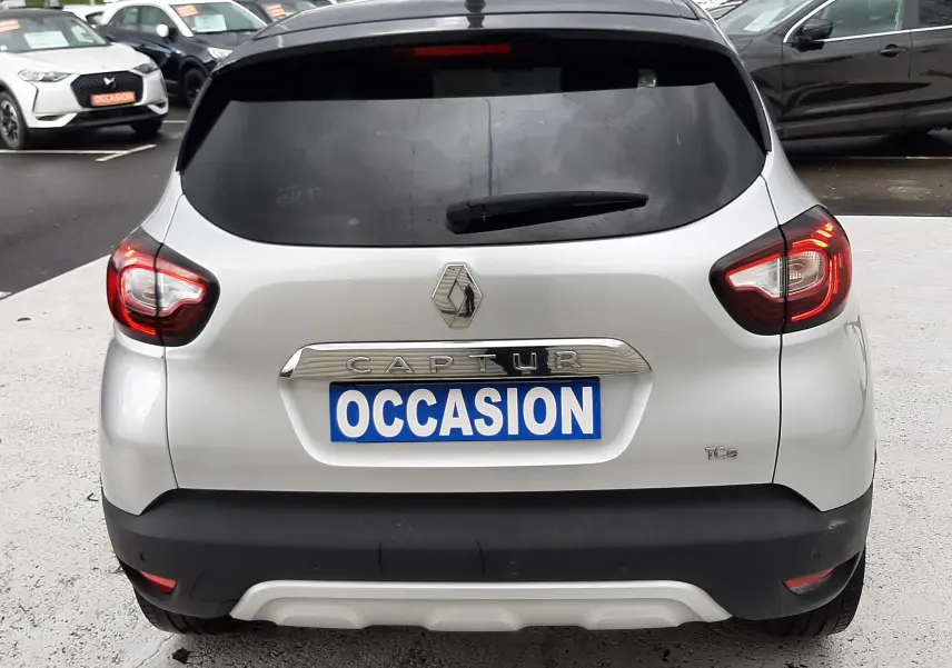 Vue arrière d'un Renault Captur gris avec toit noir, feux allumés et plaque "OCCASION" visible.