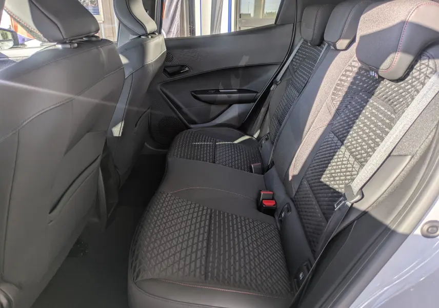 Vue intérieure arrière côté droit de la Renault Clio VI TCe 115ch Techno, sièges tissu noir avec surpiqûres rouges.