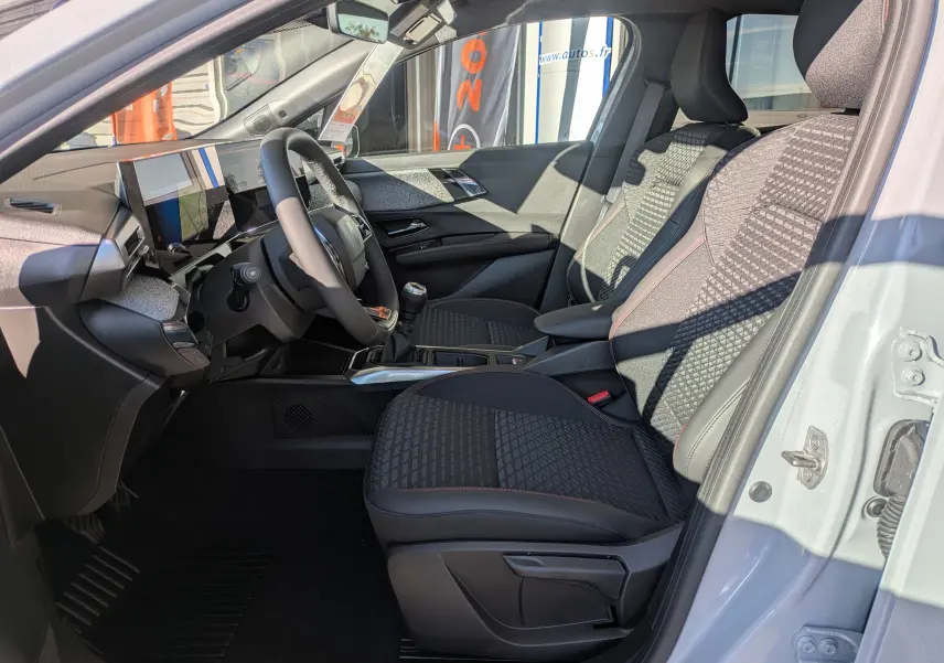Vue intérieure côté conducteur de la Renault Clio gris Rafale, sièges tissu noir avec surpiqûres rouges et tableau de bord moderne.