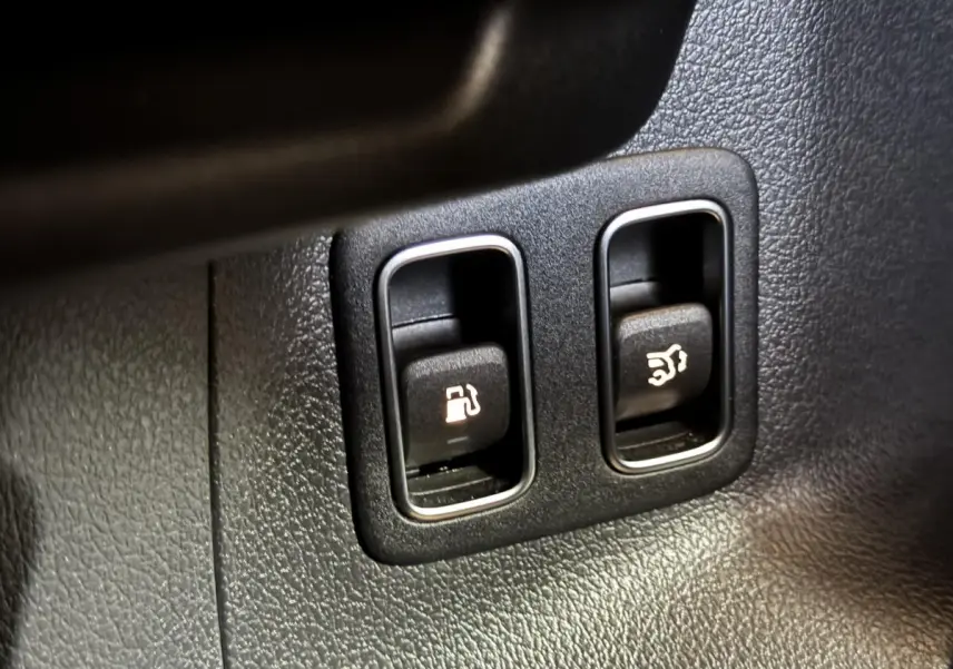 Gros plan sur les boutons d'ouverture de trappe à carburant et coffre dans un Mercedes GLA 250 e Business Line gris foncé.
