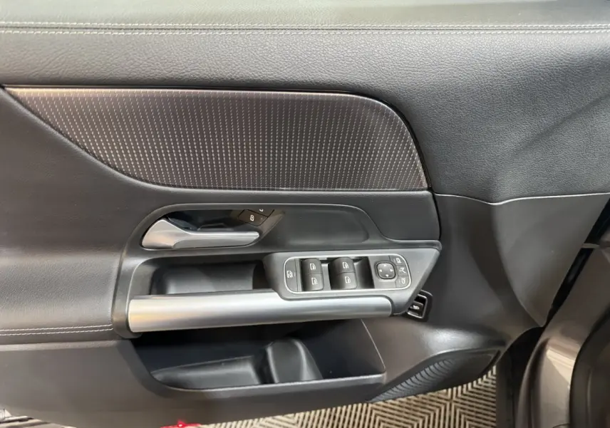 Vue intérieure du panneau de porte avant gauche gris foncé du Mercedes GLA 250 e avec commandes des vitres et poignée argentée.