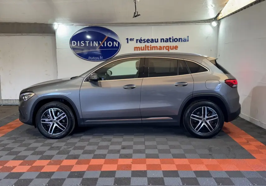 Vue de profil côté gauche d'un Mercedes GLA 250 e Business Line gris foncé, stationné en intérieur sur sol à damiers noir et orange.