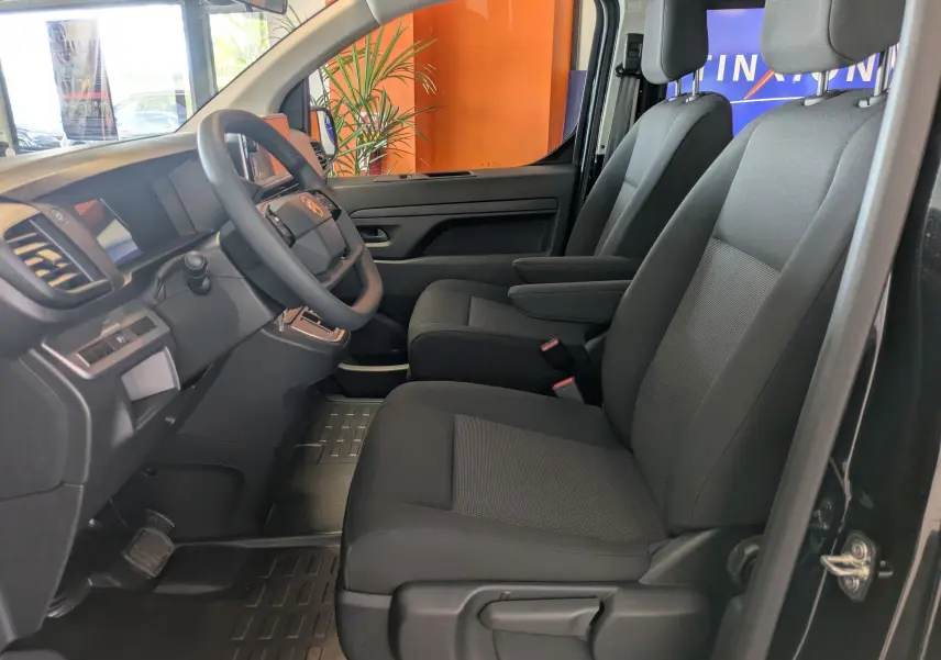 Vue intérieure côté conducteur du Citroën Jumpy Cabine Approfondie 2025, sièges tissu noir avec accoudoirs et volant multifonction.