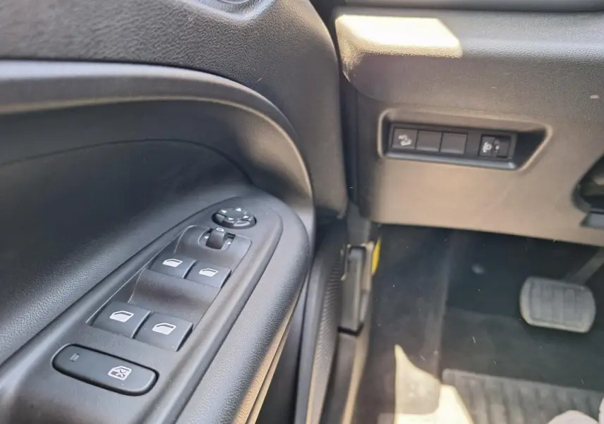 Gros plan sur les commandes des vitres électriques et rétroviseurs du côté gauche intérieur du Jeep Avenger blanc électrique 2025.