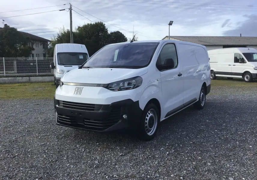 Fourgon FIAT Scudo blanc en 3/4 avant droit, avec pare-chocs noir et jantes acier, stationné sur un sol gravillonné.
