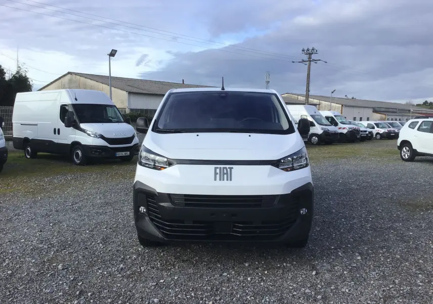 Vue de face d'un FIAT Scudo Fourgon blanc 2024 avec calandre noire et logo FIAT visible sur un parking extérieur.