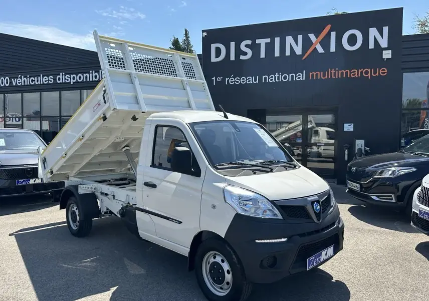 Véhicule utilitaire Piaggio Porter blanc vu en 3/4 avant droit avec benne basculante levée sur parking.