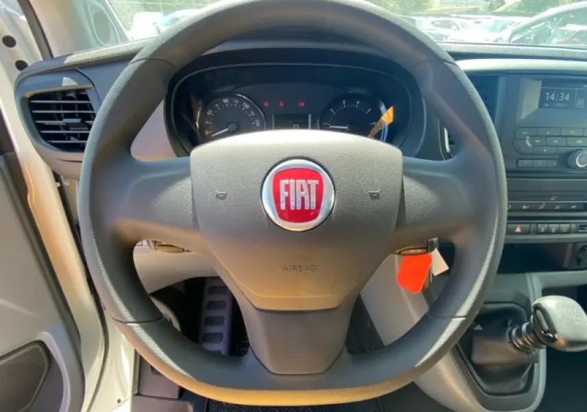 Vue intérieure centrée sur le volant noir avec logo Fiat rouge du FIAT Scudo Fourgon blanc, levier de vitesses manuel visible.