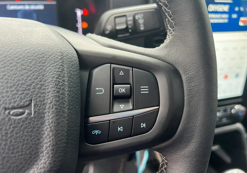 Gros plan sur les commandes au volant du Ford Ranger 2025 gris carbone, avec écran tactile en arrière-plan.