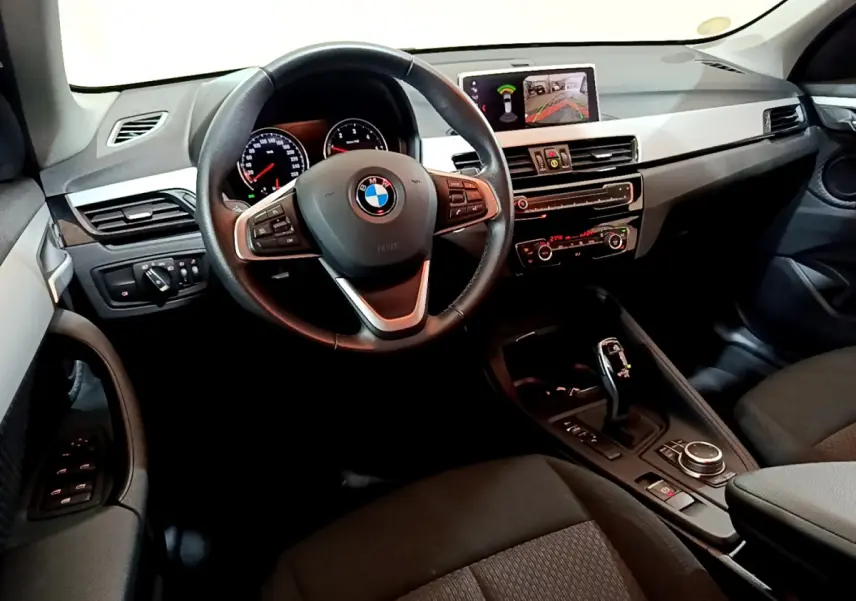 Vue intérieure côté conducteur du BMW X1 noir 2021, avec volant cuir multifonctions et écran central affichant la caméra de recul.