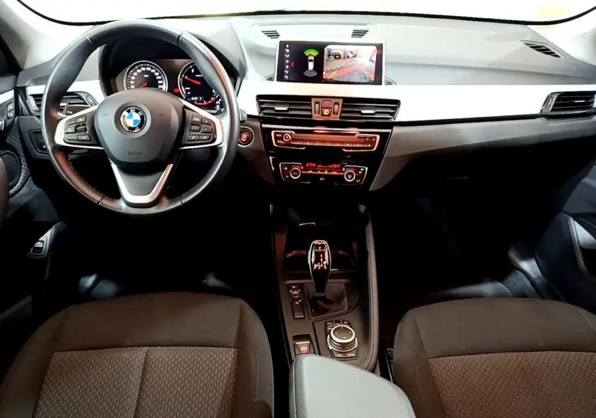Vue intérieure avant du BMW X1 2021 noir, tableau de bord avec écran central affichant la caméra de recul.