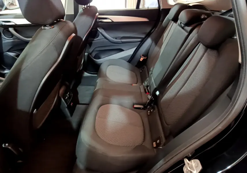 Vue intérieure côté droit des sièges arrière noirs en tissu du BMW X1 sDrive16d Lounge 2021, avec portes ouvertes.