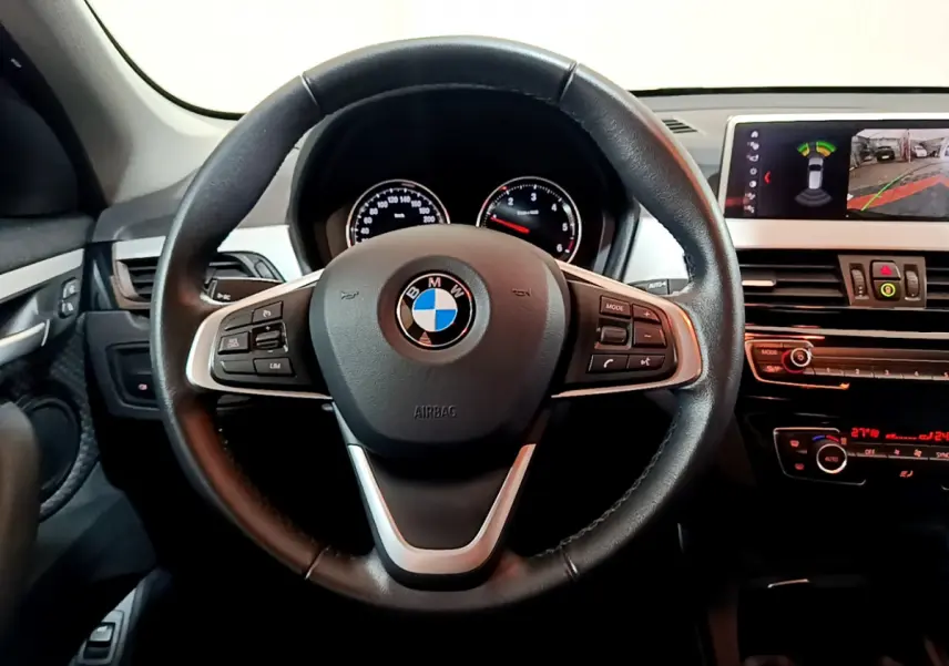 Vue intérieure centrée sur le volant cuir multifonctions d'une BMW X1 2021 avec tableau de bord et écran multimédia.