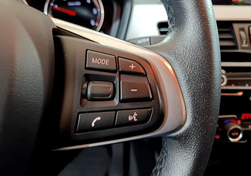 Gros plan sur les commandes gauche du volant cuir noir du BMW X1 2021, avec tableau de bord en arrière-plan.