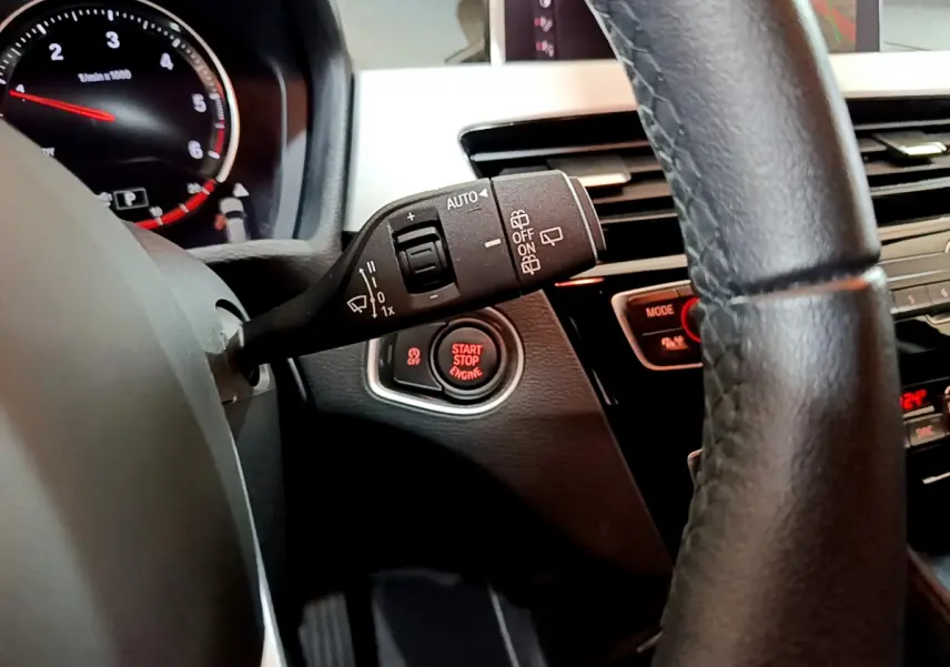 Détail intérieur du BMW X1 2021 noir montrant le commodo d’essuie-glace, bouton start/stop et partie du volant cuir.