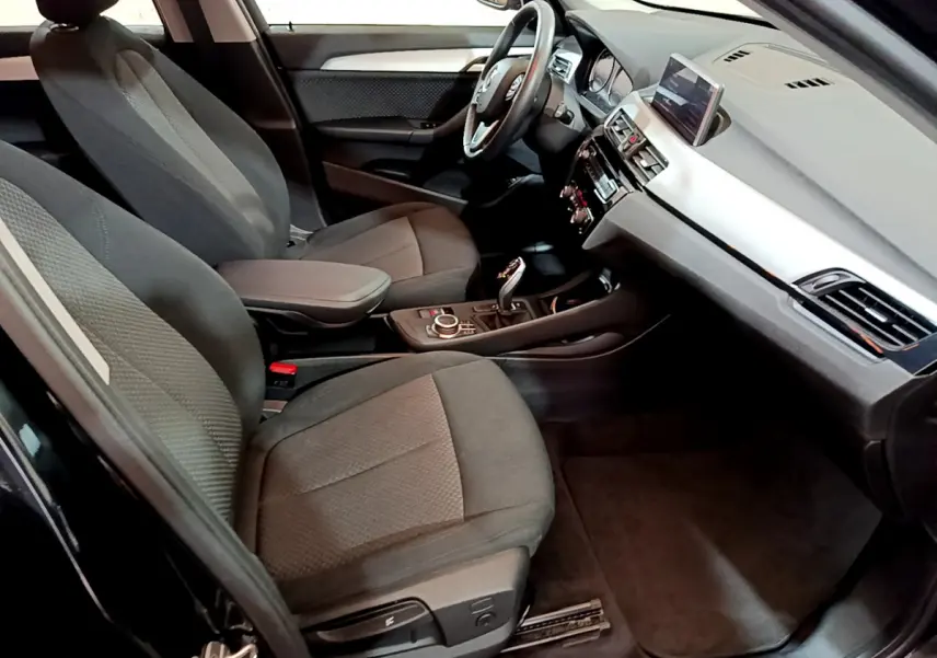 Vue intérieure côté conducteur de la BMW X1 sDrive16d Lounge 2021 avec sièges tissu gris et tableau de bord moderne.