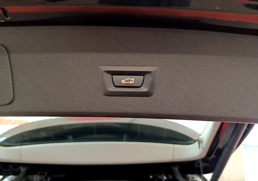 Gros plan sur le bouton d'ouverture électrique du coffre, intérieur du hayon noir du BMW X1 sDrive16d Lounge 2021.