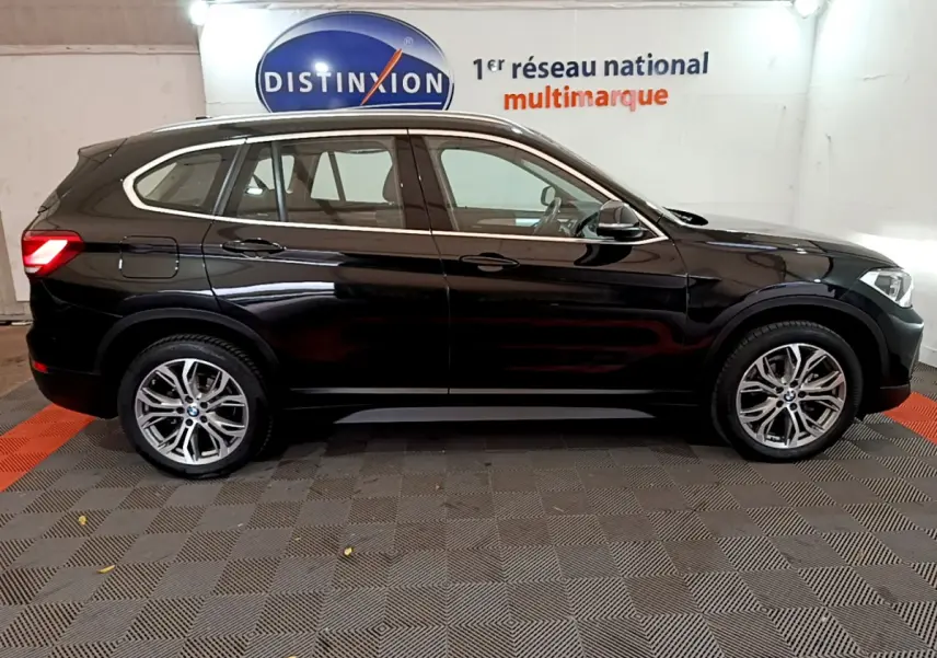 BMW X1 sDrive16d noir vue de profil côté gauche, stationné en intérieur avec jantes alliage visibles.