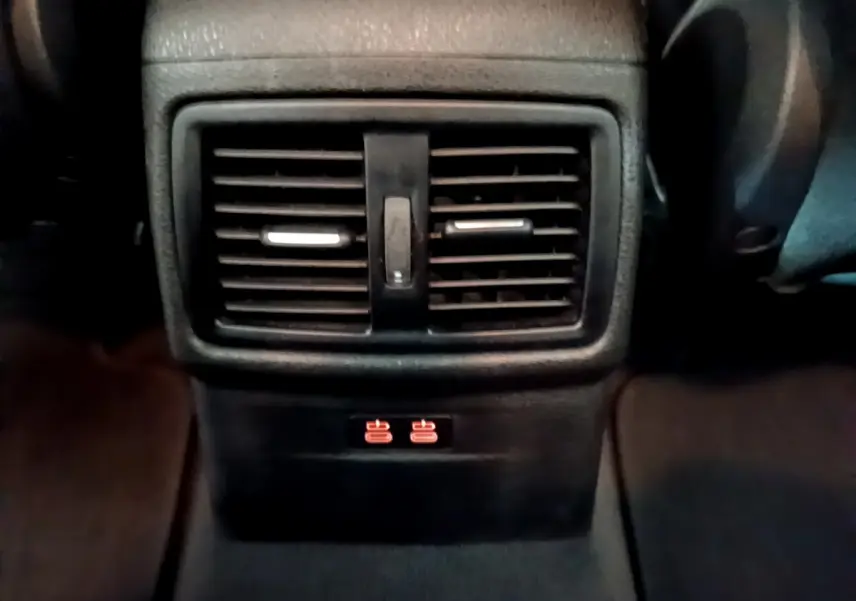 Détail des aérateurs arrière noirs avec commandes de chauffage rouge sur la console centrale d'un BMW X1 noir.