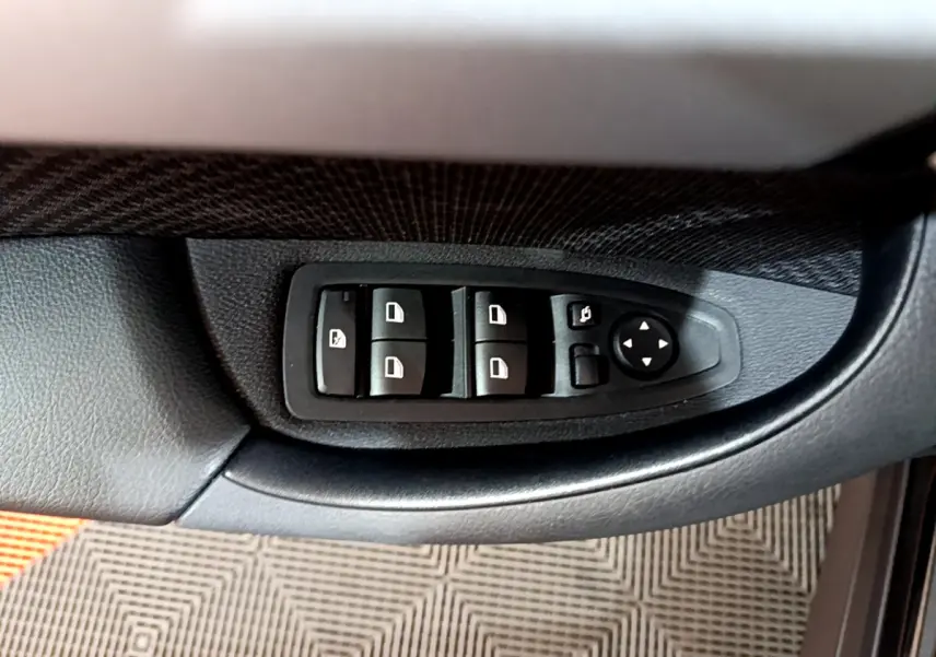 Gros plan sur les commandes de lève-vitres et rétroviseurs côté conducteur d'une BMW X1 noire 2021.