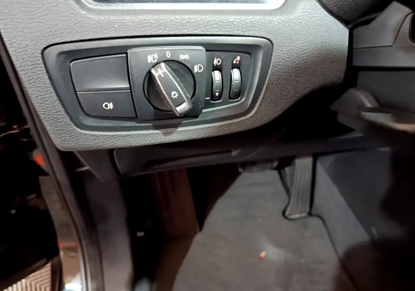 Détail du tableau de bord noir du BMW X1 sDrive16d Lounge 2021, avec commandes d’éclairage et pédale visible.
