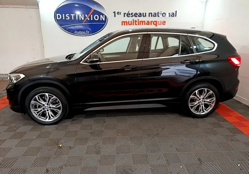 BMW X1 sDrive16d noir vue de profil côté gauche, avec jantes alliage et rétroviseurs électriques dans un showroom.