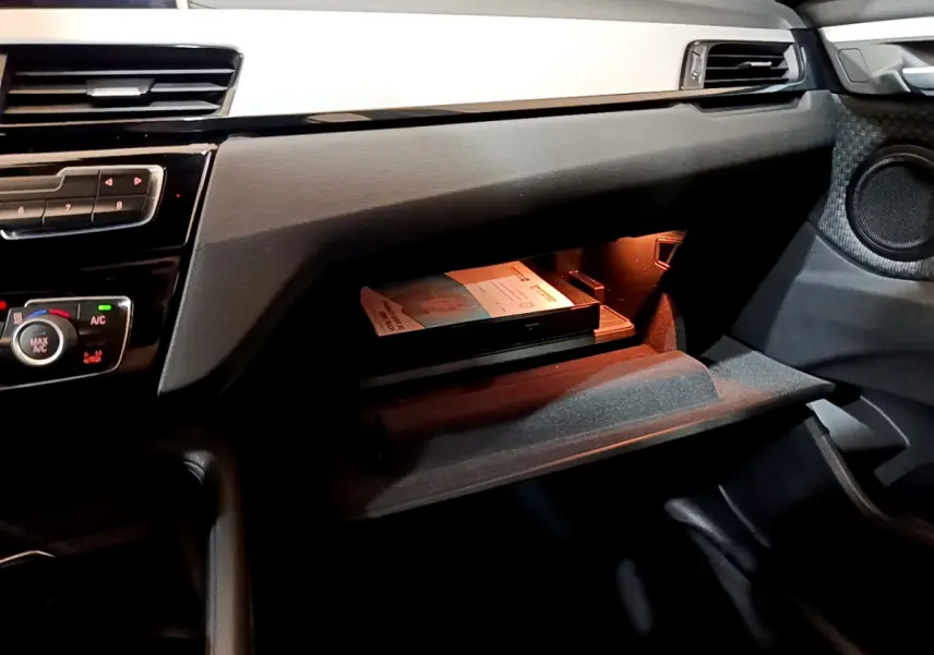 Gros plan sur la boîte à gants ouverte du BMW X1 sDrive16d Lounge 2021, intérieur noir avec éclairage intérieur.