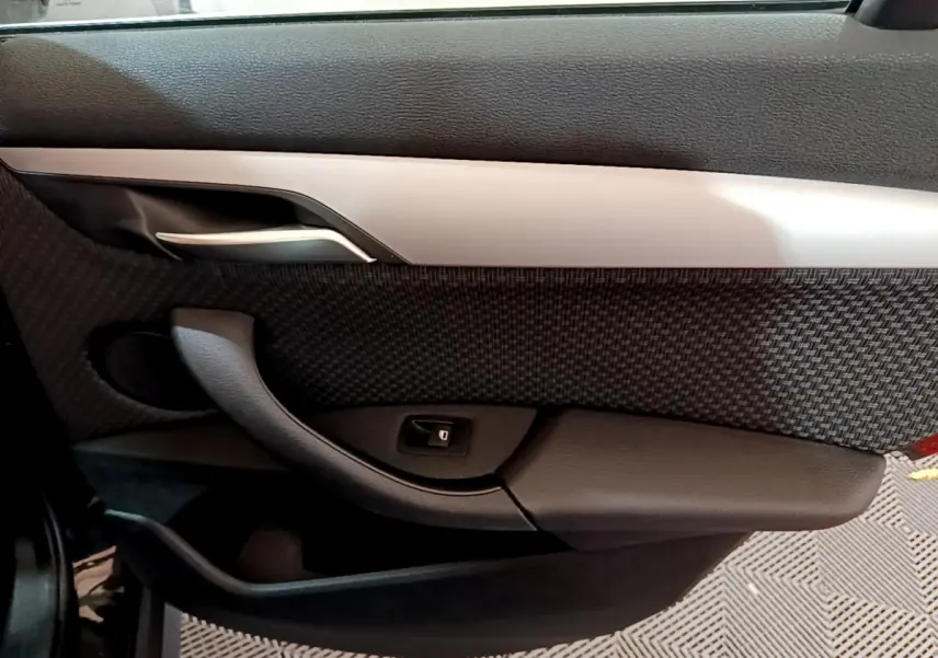 Vue intérieure du panneau de porte côté gauche de la BMW X1 sDrive16d Lounge 2021, avec insert tissu et poignée argentée.
