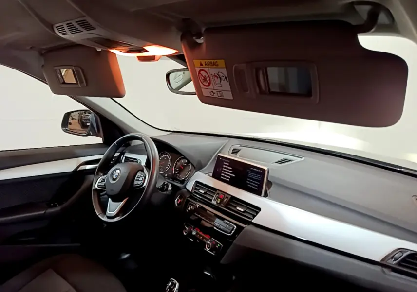 Vue intérieure côté conducteur du BMW X1 2021, tableau de bord avec écran central et volant cuir multifonctions.