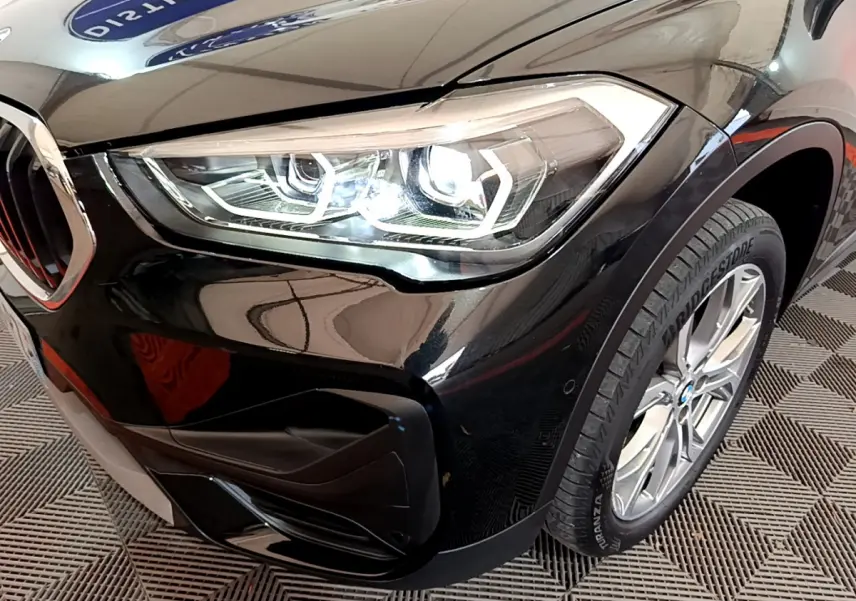 Gros plan sur l'avant droit noir brillant du BMW X1 sDrive16d 2021, mettant en valeur le phare LED et la roue.