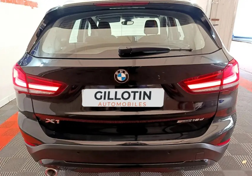 Vue arrière d’un BMW X1 sDrive16d noir avec feux LED allumés et logo visible sur un sol à damier rouge et gris.