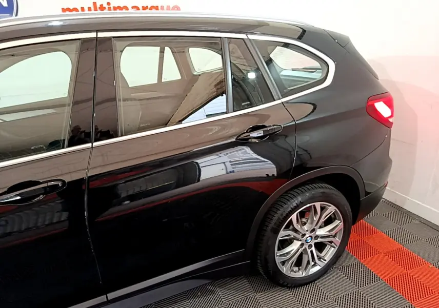 Vue latérale droite d'un BMW X1 noir 2021 avec jante alliage et feu arrière allumé dans un garage.