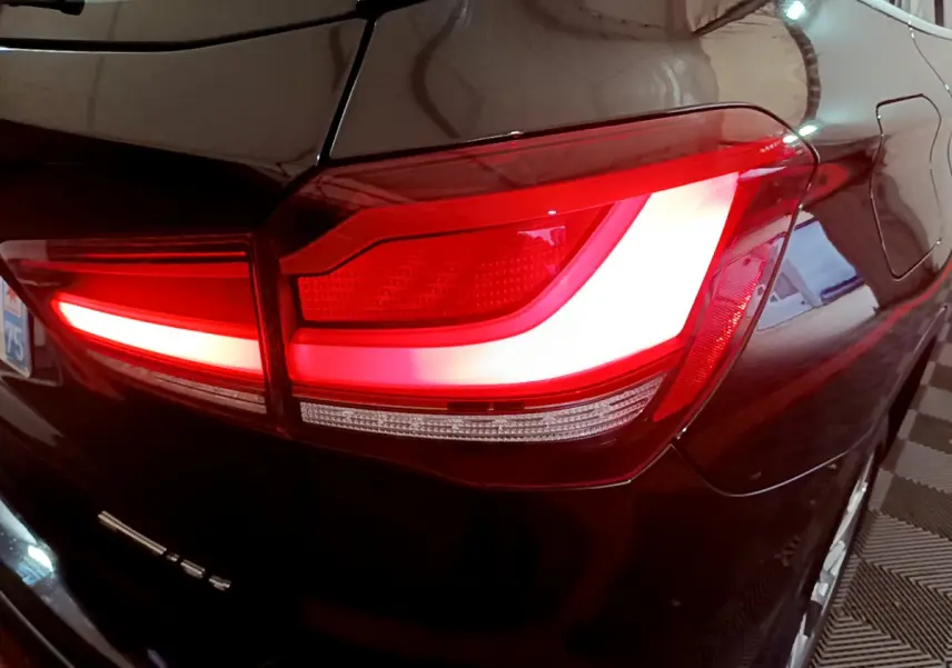 Gros plan sur le feu arrière droit rouge et blanc d’un BMW X1 noir, avec reflet sur la carrosserie brillante.