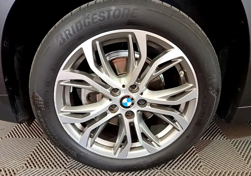 Gros plan sur la roue avant droite d’un BMW X1 noir, jante alliage argentée à design multiple branches.