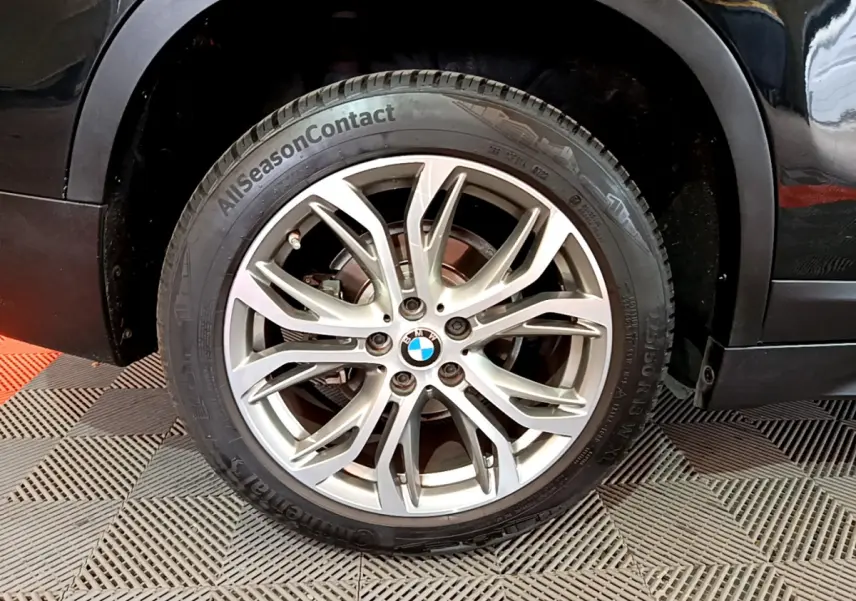 Gros plan sur la roue avant gauche avec jante alliage argentée et logo BMW sur BMW X1 noir sDrive16d Lounge DKG7.