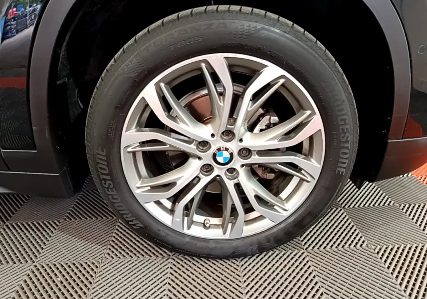 Gros plan sur la roue avant droite noire d’un BMW X1 2021 avec jante alliage multi-branches argentée.